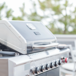 Stainless steel grill and outdoor kitchen appliances installed on a bright backyard patio.