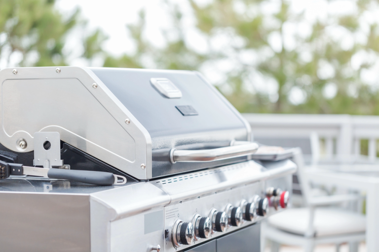 Stainless steel grill and outdoor kitchen appliances installed on a bright backyard patio.